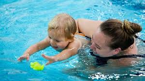 Parent playing with baby in the pool with floating toys