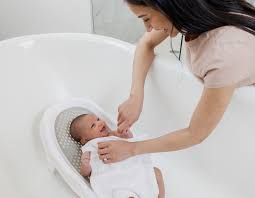 Parent testing bath water temperature while baby sits nearby
